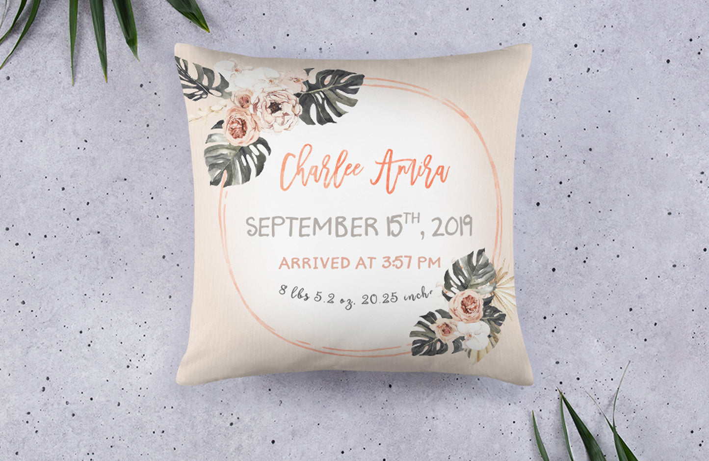 Modern tropics themed birth announcement pillow that says the baby's name, date and time of birth, weight, and length. It is orange and beige with flowers and leaves in the two opposite corners.